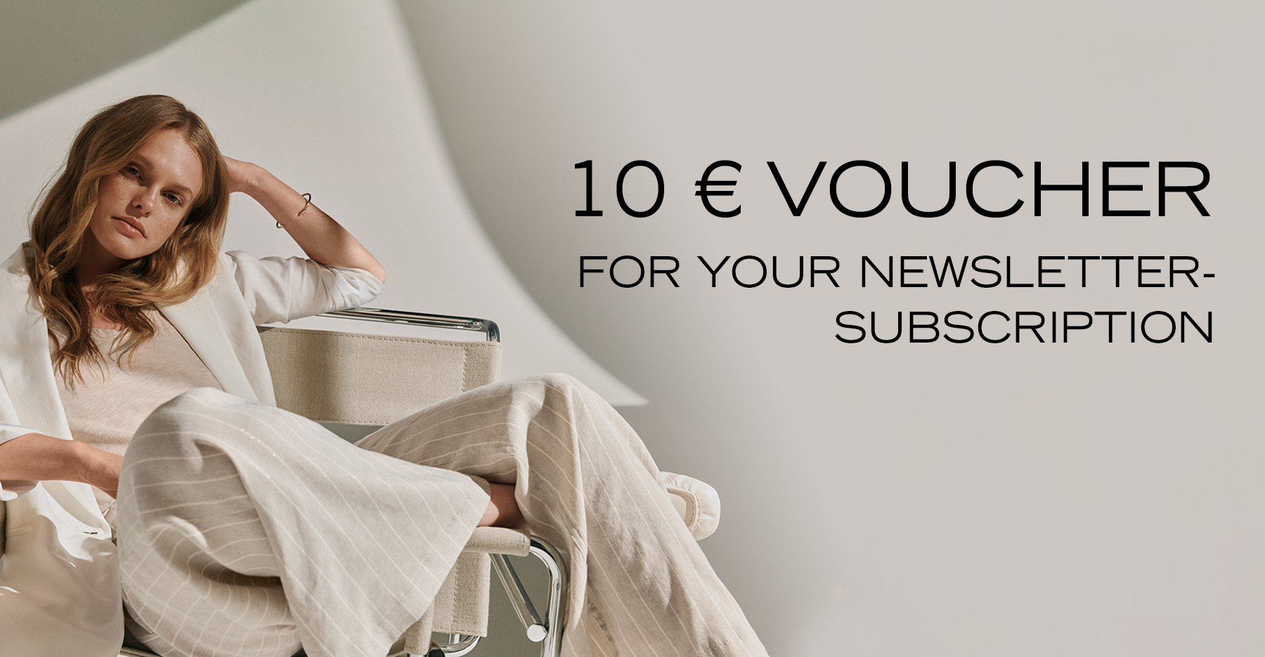 Woman in light, flowing fabrics sitting relaxed in a designer chair – teaser for newsletter sign-up with €10 voucher.