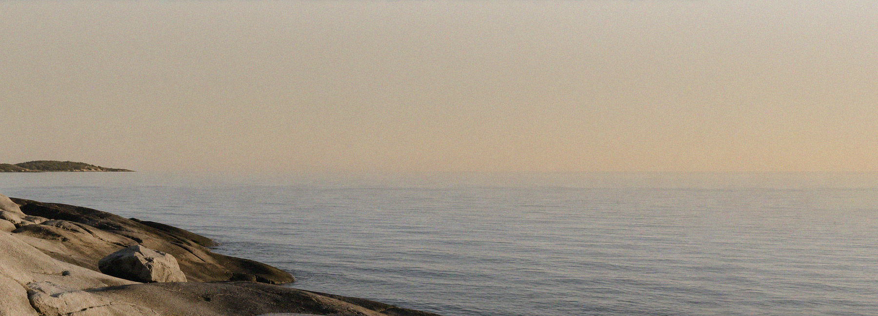 Expansive coastal landscape with sea and rocky shoreline in warm light – hero banner for the ROSNER Studio Sale