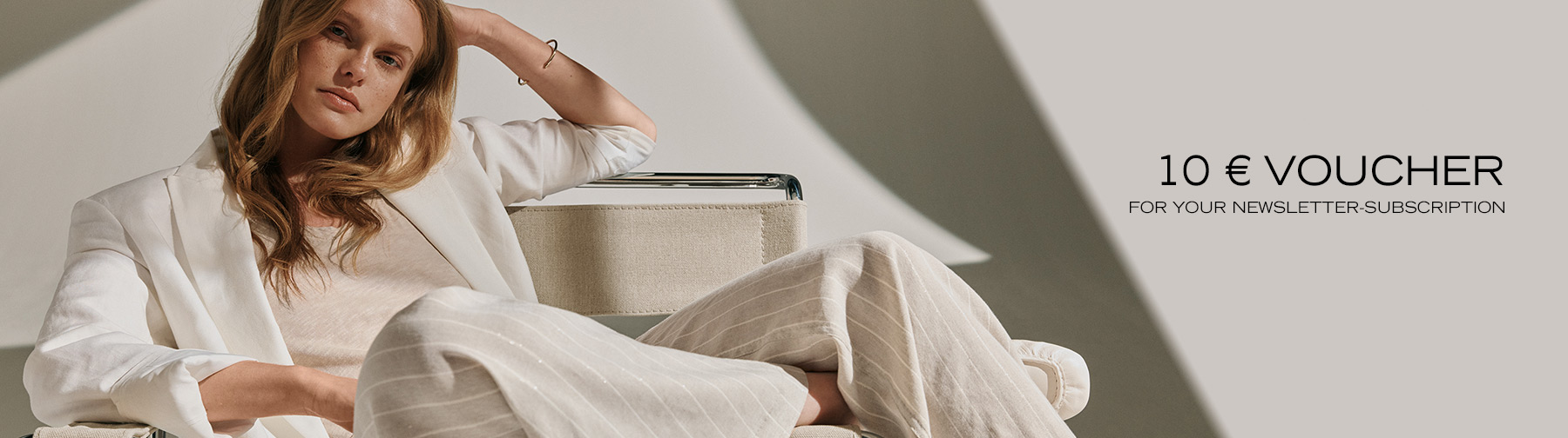 Woman in light, flowing fabrics sitting relaxed in a designer chair – teaser for newsletter sign-up with €10 voucher.