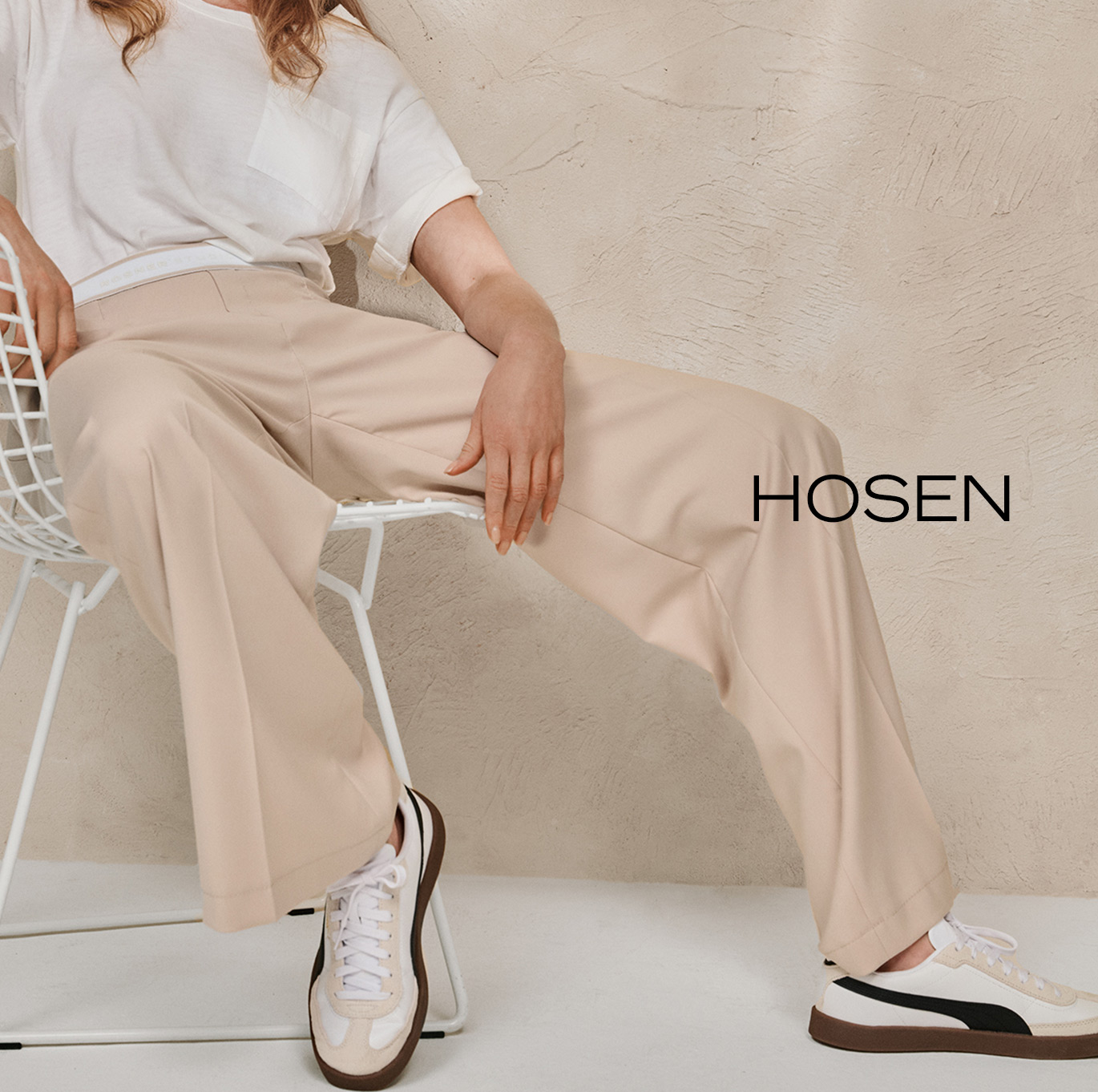 Modell in weiter beigefarbener Hose und weißem Shirt auf Stuhl sitzend – Teaser zur Kategorie Hosen von ROSNER