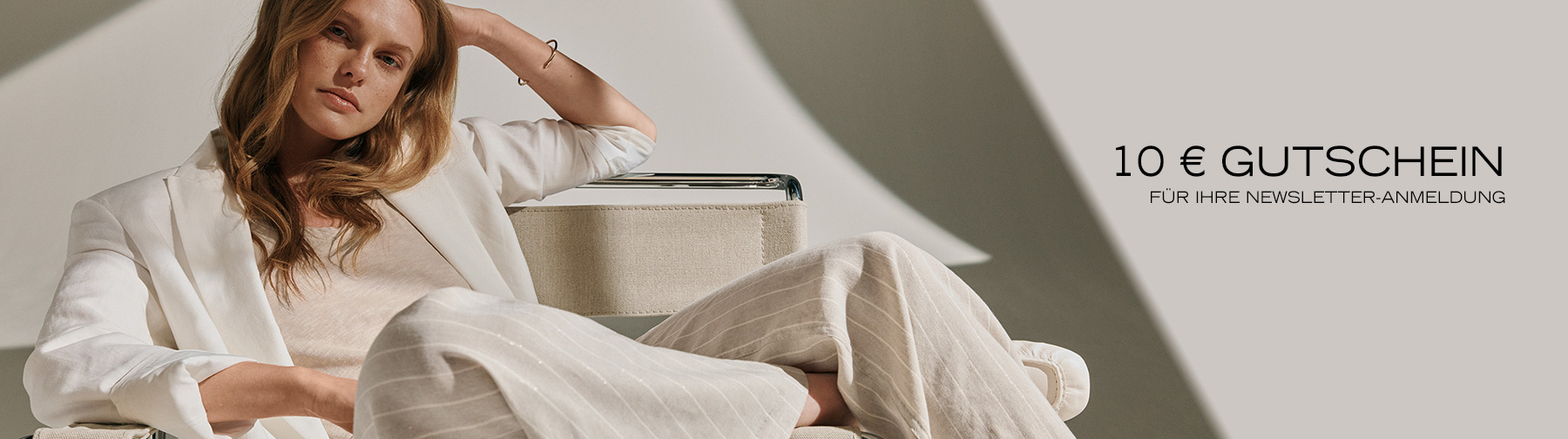 Frau in hellen, fließenden Stoffen sitzt entspannt im Designstuhl – Teaser zur Newsletter-Anmeldung mit 10 € Gutschein.