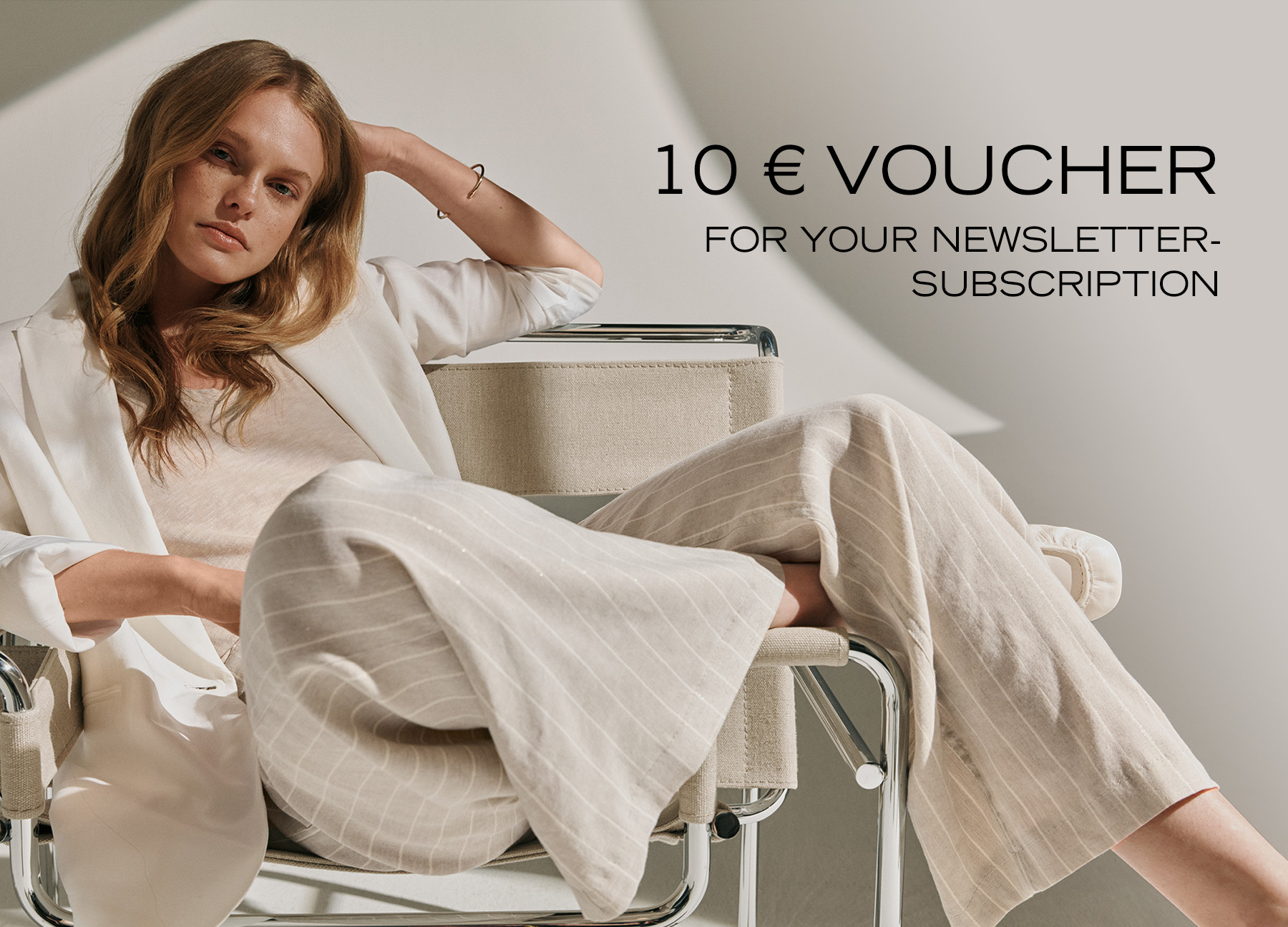 Woman in light, flowing fabrics sitting relaxed in a designer chair – teaser for newsletter sign-up with €10 voucher.
